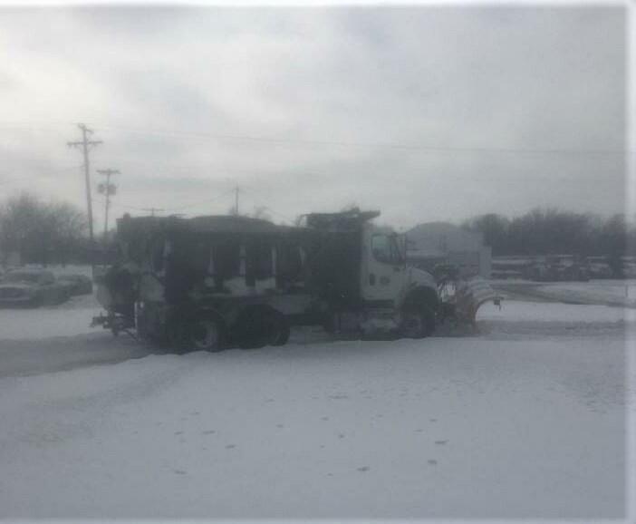 Large plow truck clearing snow from parking lot.